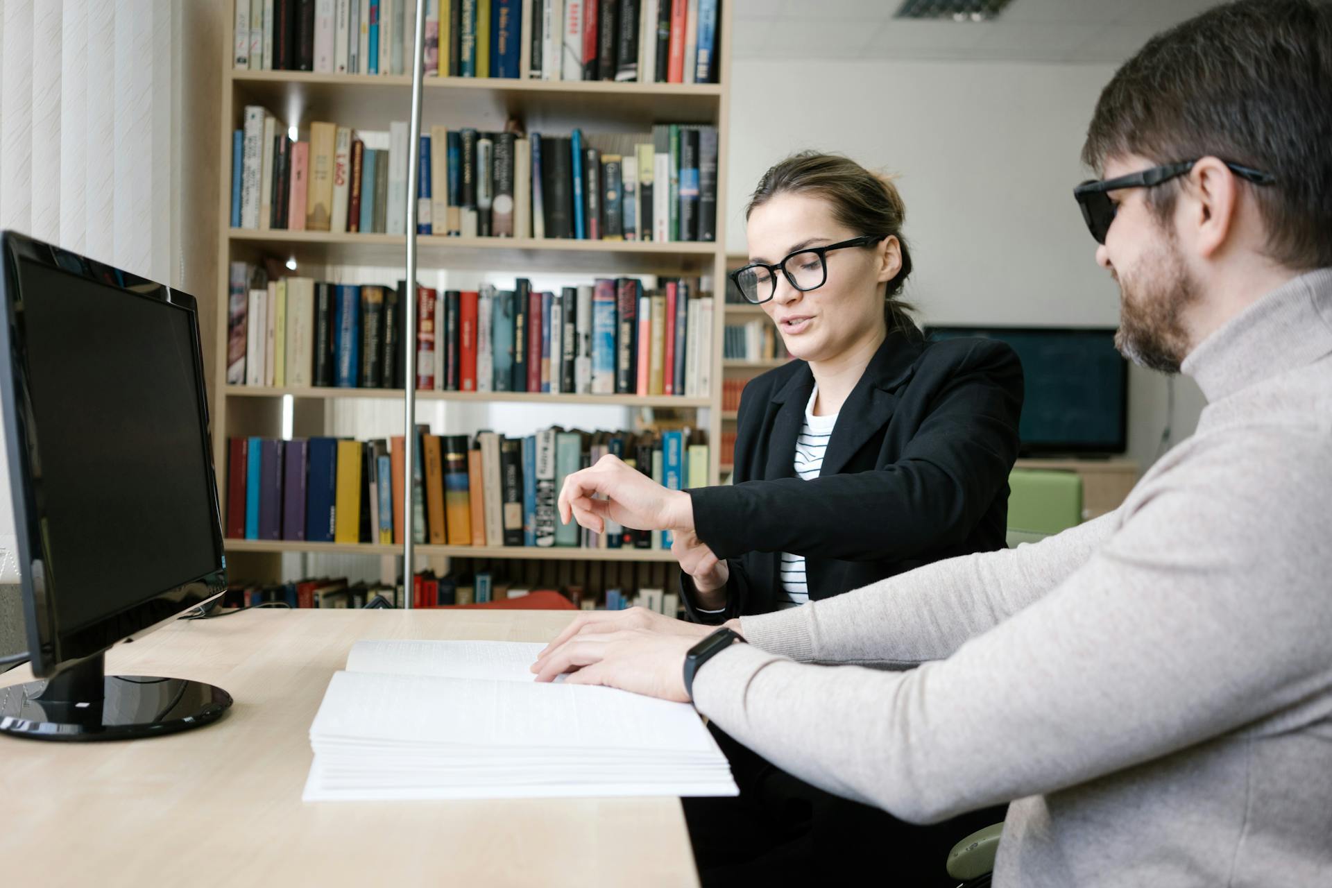 Dans un bureau, une femme écoute un homme qui lit un livre en braille